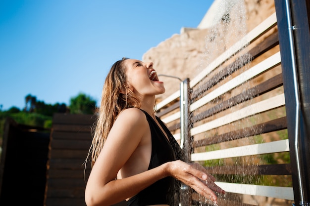 Beautiful young  girl dressed in swimwear taking a shower on beach