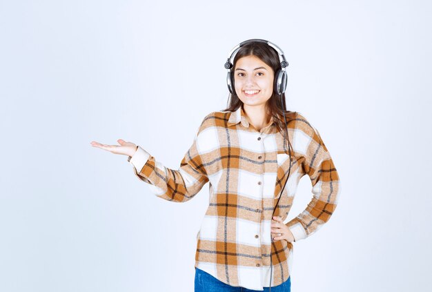 Beautiful young girl in headphones listening to song over white wall. 