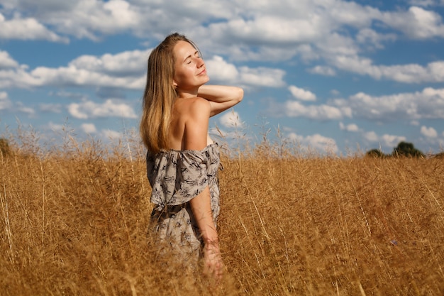 Beautiful young girl  is on wheat field in sunny day. an seductive girl with long light  hair walk in the wheat field happy girl in  field with spikelets landscape. weekend outdoors in summer.