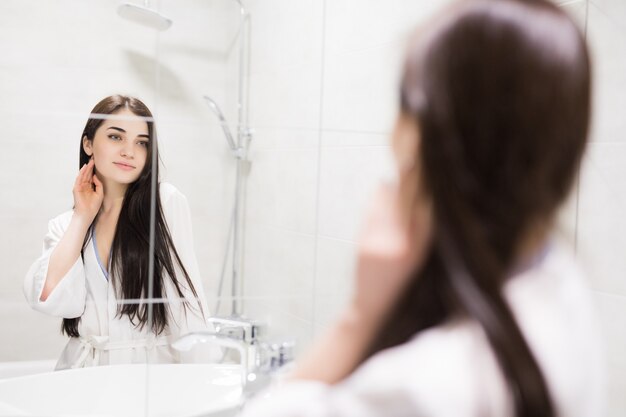 Красивая молодая девушка, глядя на отражение в зеркале, оставаясь в ванной комнате