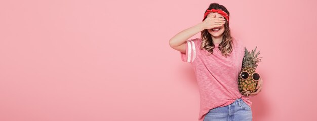 ピンクのtシャツの美しい少女は彼女の顔を覆い、パイナップルを保持