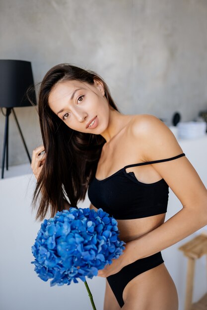 Beautiful young girl posing in lingerie in the living room. Fashion portrait model in living room with blue flowers.