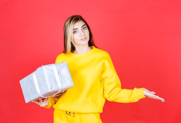 Beautiful young girl posing with gift box on red wall