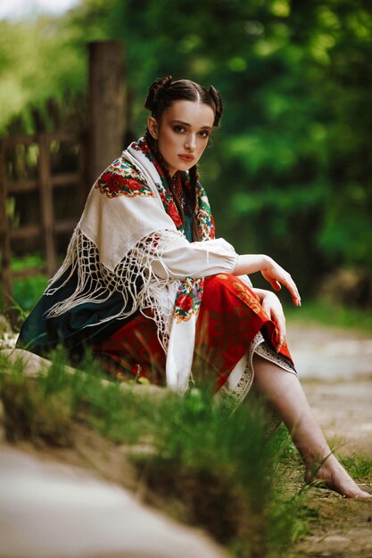 カラフルなウクライナのドレスで公園に座っている美しい少女