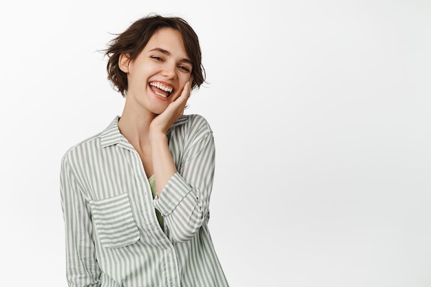 Beautiful young girl touching clean healthy skin, laughing and smiling happy, standing over white background.