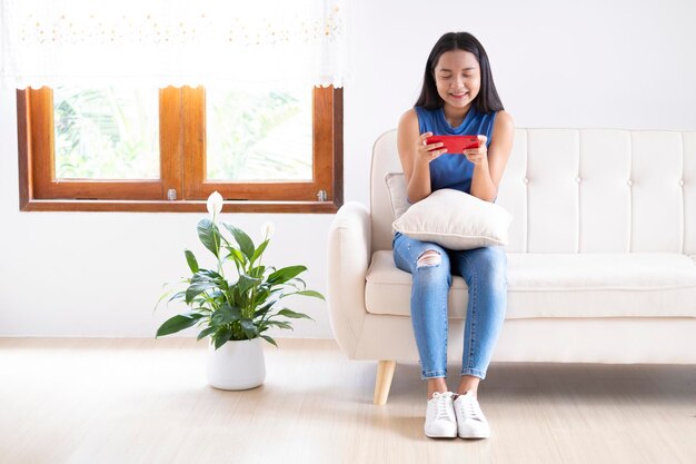 Beautiful young girl use smartphone sitting on sofa at home