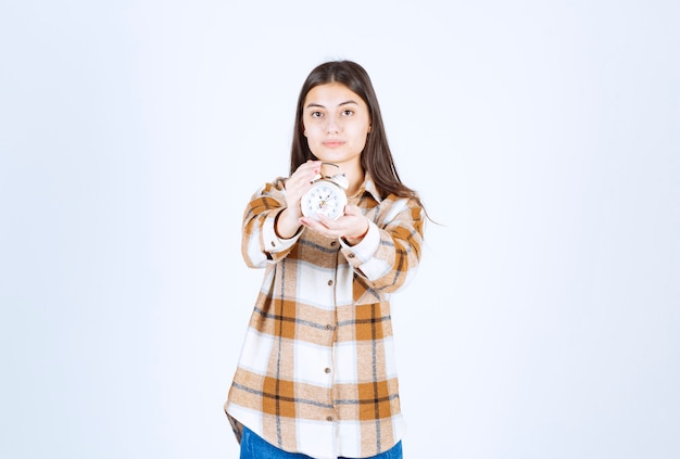 Free photo beautiful young girl wearing casual clothes showing alarm clock.