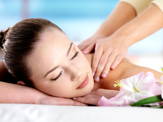 Beautiful young girl with attractive face having a massage for  shoulder on resort - colored space