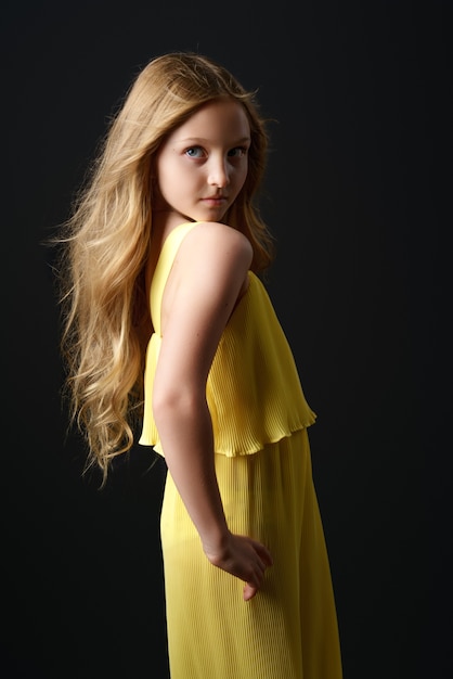Красивая молодая девушка с распущенными волосами в модной желтой одежде позирует на черном фоне