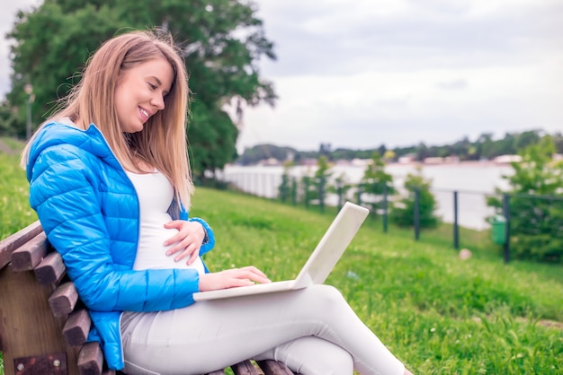 Bella ragazza che lavora con il computer portatile godendo di connettività eccellente nel mezzo del parco. donna incinta utilizzando il suo computer portatile all'aperto. donna on line navigare i social media