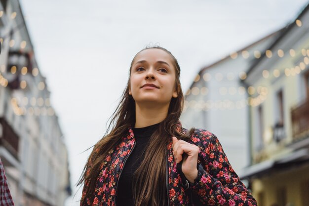 屋外でポーズを取る長い髪と美しい若い幸せなブルネットの女の子。ストリート写真、ポートレート、クローズアップ。