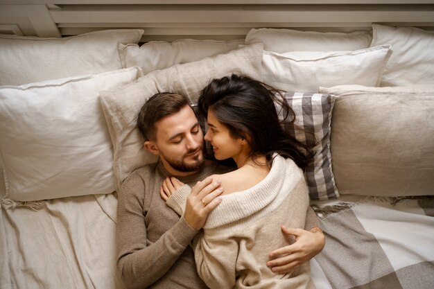 Beautiful young happy couple relaxing in bed and smiling, embracing