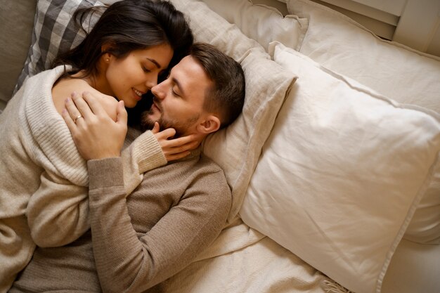 ベッドでリラックスし、笑顔で抱きしめて美しい若い幸せなカップル