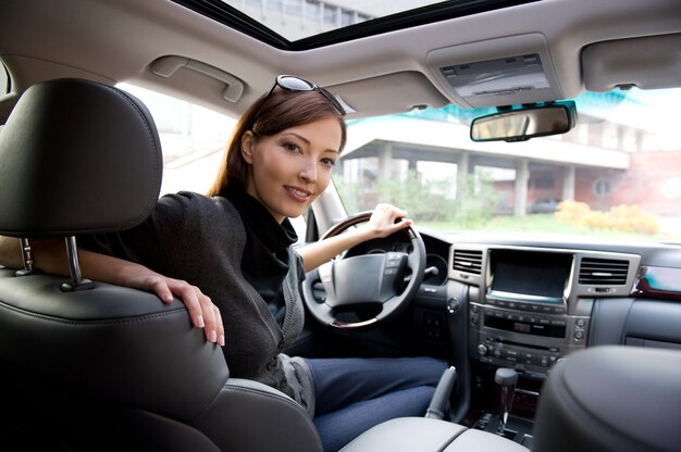 新しい車の中でポーズをとって美しい若い幸せな女性