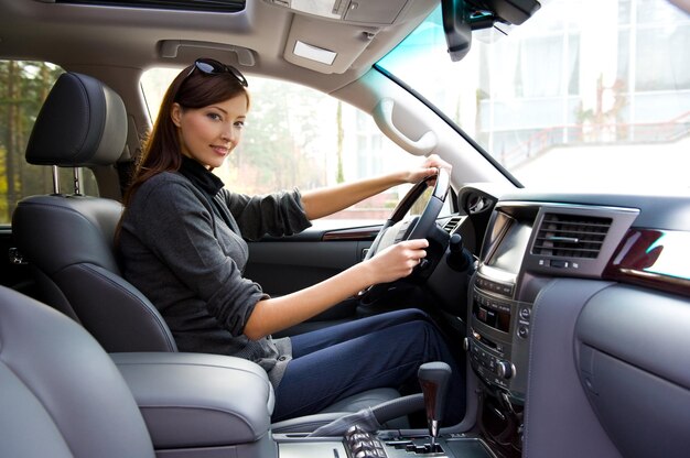 新しい車の中でポーズをとって美しい若い幸せな女性