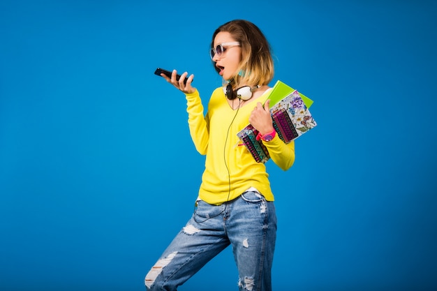 Beautiful young hipster woman holding books and looking at smartphone