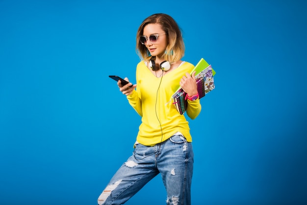 Beautiful young hipster woman holding books and looking at smartphone