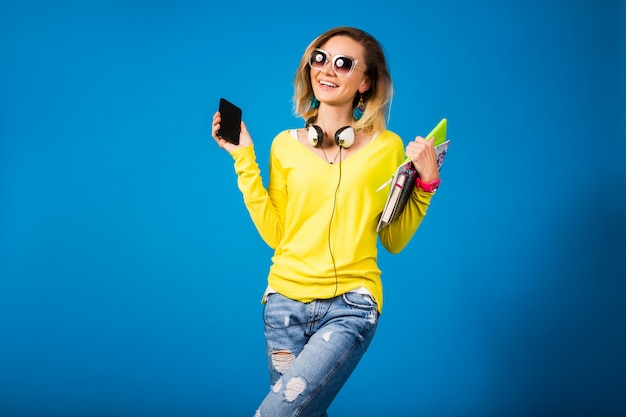 Beautiful young hipster woman holding books and looking at smartphone