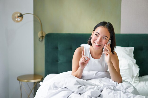 Beautiful young korean woman calling having a phone call in bed talking with friend while staying in