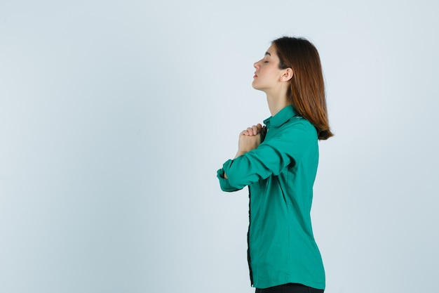 Beautiful young lady clasping hands in praying gesture in green shirt and looking hopeful .