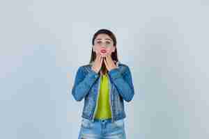 Free photo beautiful young lady in denim outfit keeping hands on chin and looking agitated , front view.