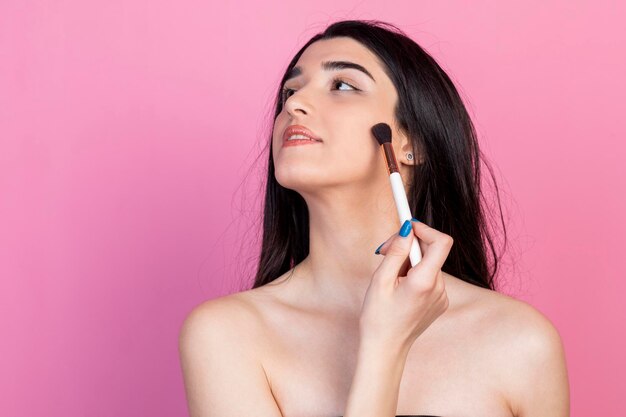 Beautiful young lady doing makeup on pink background High quality photo