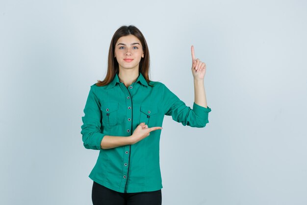 Beautiful young lady in green shirt pointing up and right and looking confident , front view.