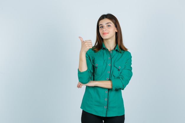 緑のシャツを着た美しい若い女性が親指を立てて自信を持って、正面図を表示します。