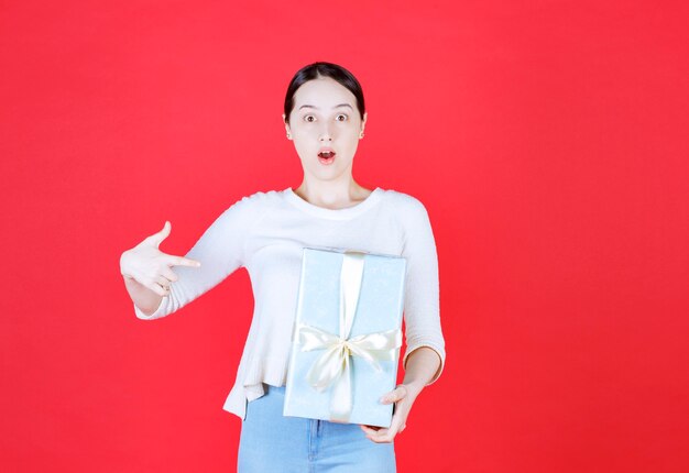 Beautiful young lady holding gift box and point finger on it