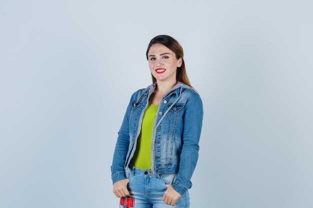 Beautiful young lady holding thumbs in pockets in denim outfit and looking confident. front view.