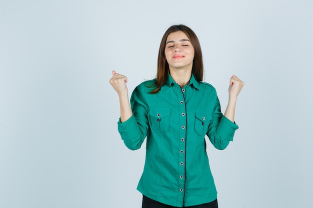 Beautiful young lady showing winner gesture in green shirt and looking lucky , front view.