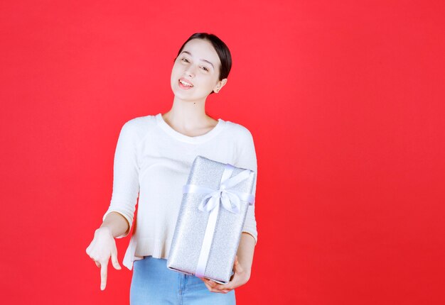 Beautiful young lady smiling and holding wrapped gift box