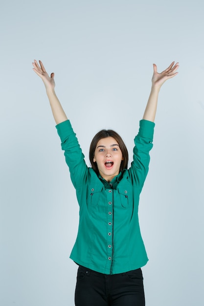 Beautiful young lady stretching arms, opening mouth in green shirt and looking blissful. front view.