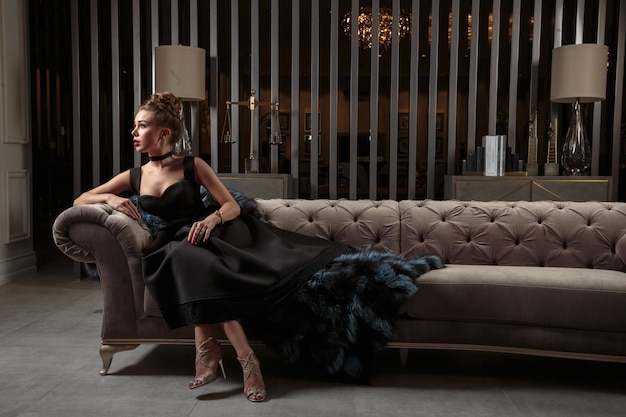 Beautiful Young Lady in Black Dress Sitting on Sofa