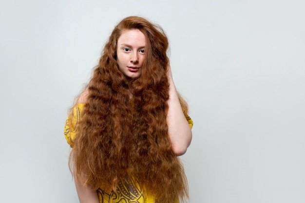 beautiful young lady with long ginger hair in yellow dress on gray