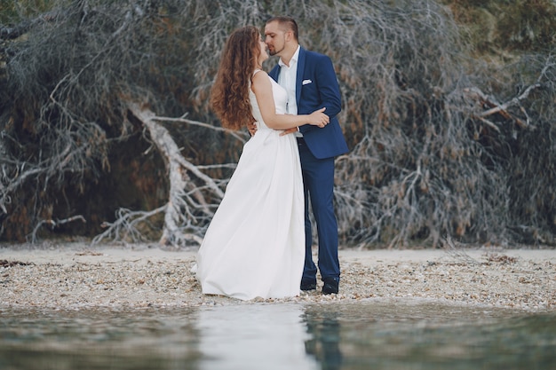 beautiful young long-haired bride in white dress with her young husband on the beach