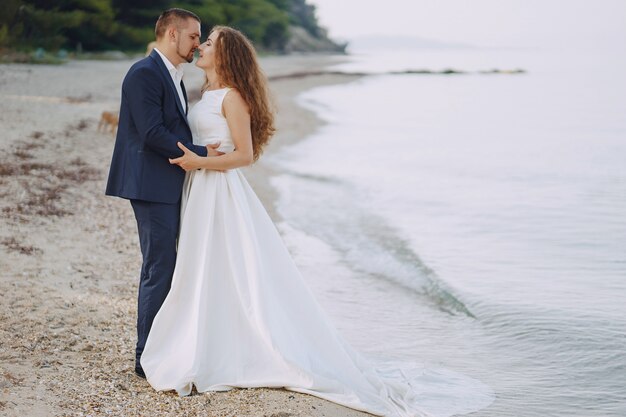 해변에서 그녀의 젊은 남편과 하얀 드레스를 입고 아름다운 젊은 긴 머리 신부