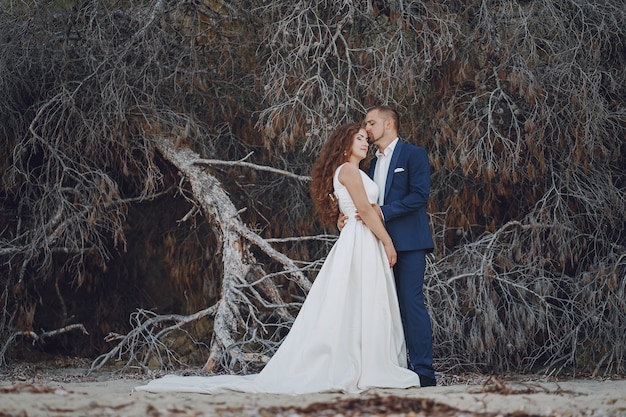 나뭇 가지 근처에 그녀의 젊은 남편과 흰 드레스에 아름 다운 젊은 긴 머리 신부