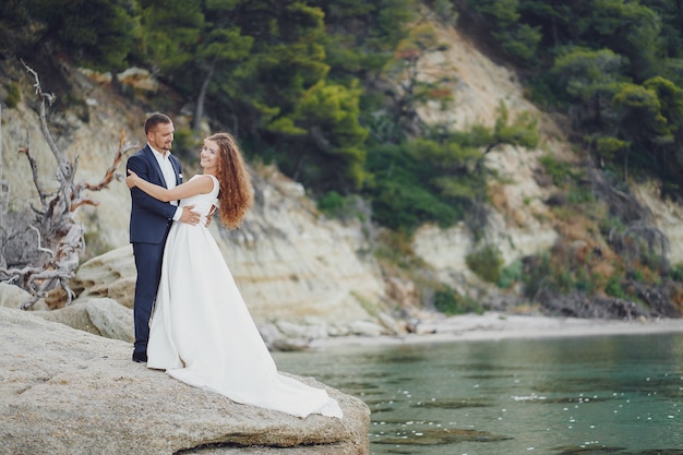 beautiful young long-haired bride in white dress with her young husband near river