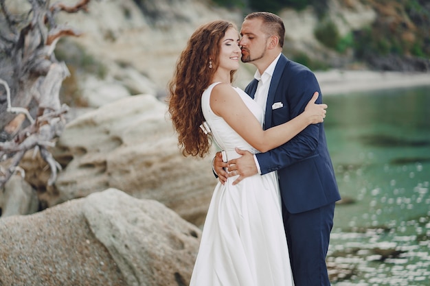 beautiful young long-haired bride in white dress with her young husband near river