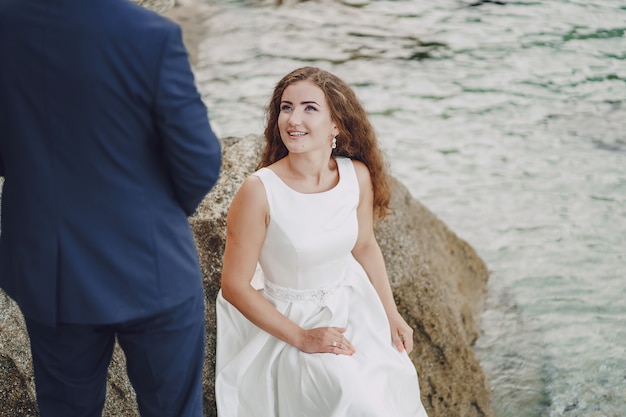 beautiful young long-haired bride in white dress with her young husband near river