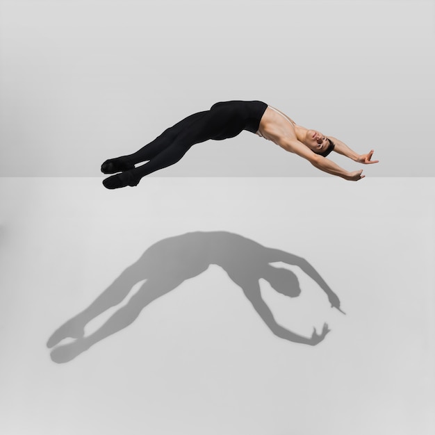 Beautiful young male athlete practicing on white studio with shadows in jump, air flying