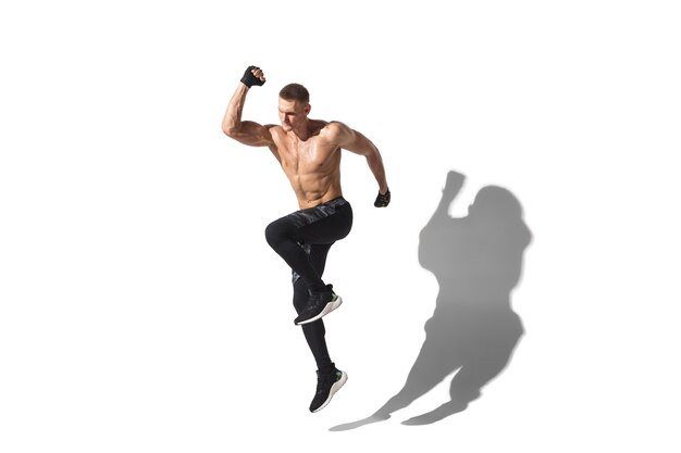 Beautiful young male athlete practicing on white studio with shadows