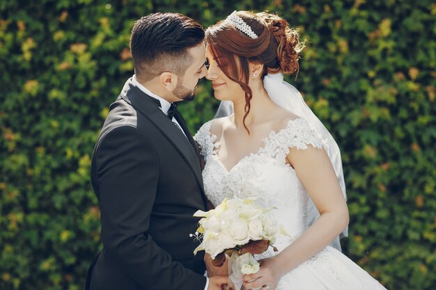 A beautiful young man wearing a black suit and a beard in the park along with his bride