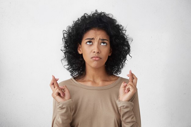 Beautiful young mixed race female student wearing long sleeved t-shirt keeping fingers crossed