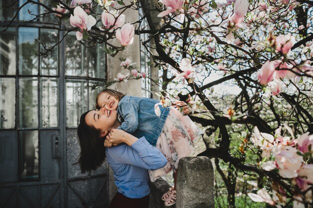 아름 다운 젊은 엄마 피 핑크 나무 아래 서 사랑스러운 작은 딸을 보유