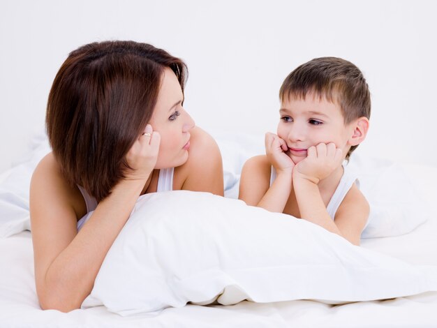 Beautiful young mother and the son look against each other lying in a bed
