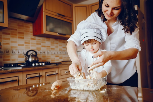 A beautiful young mother with her little daughter is cooking in the kitchen at home