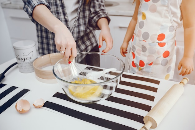 A beautiful young mother with her little daughter is cooking in the kitchen at home