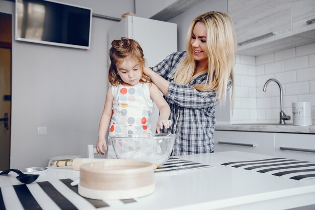 彼女の小さな娘と美しい若い母親は家庭の台所で料理しています